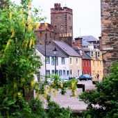 visit_scotland_-_looking_past_cars_to_a_couple_walking_on_a_cobbled_street_in_kirkcudbright