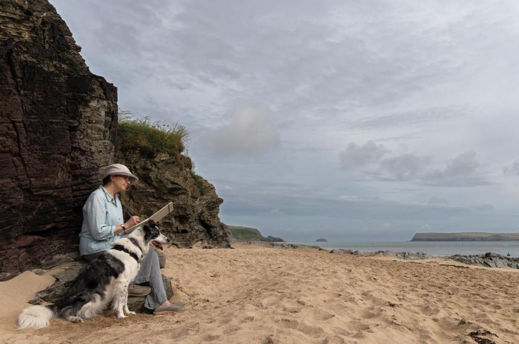Perched on limpet-strewn tidal rocks, artist Sarah Adams sketches the Cornish landscape with her border collie, Dab, by her side. Harmony Murt